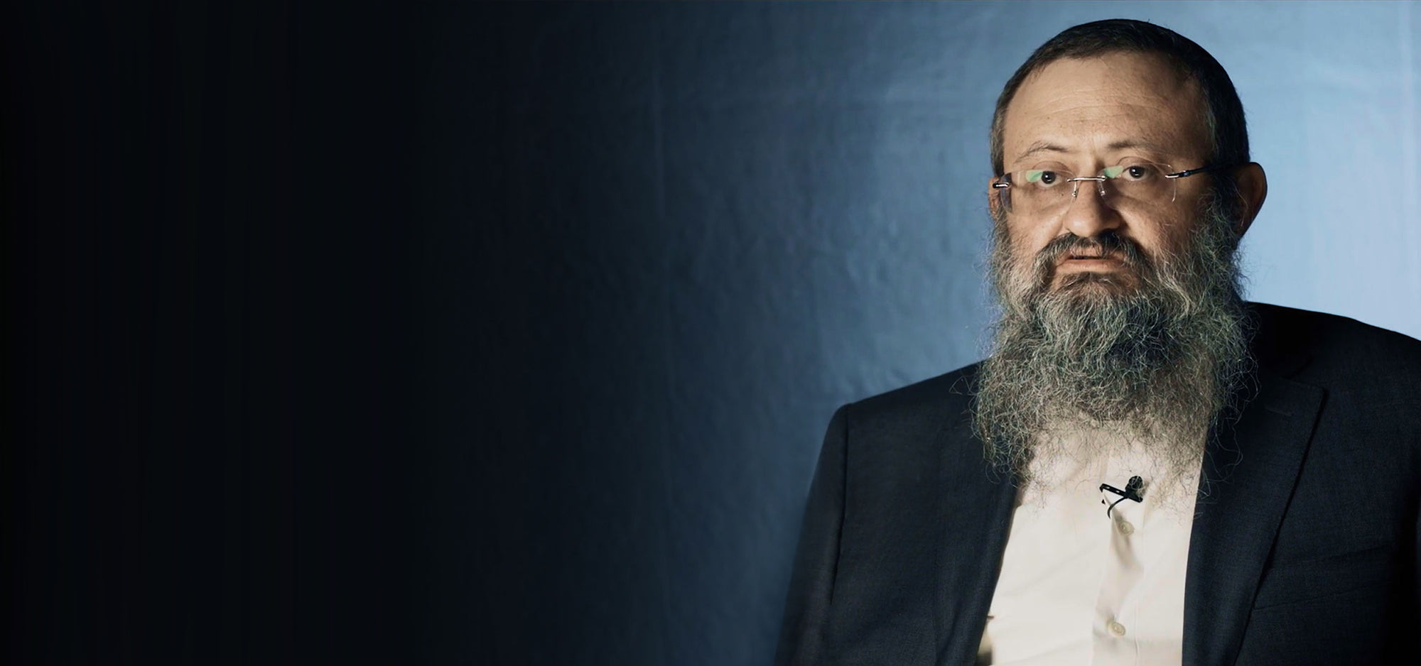 Doctor Zelenko, a man with a beard and glasses wearing a suit against a dark background